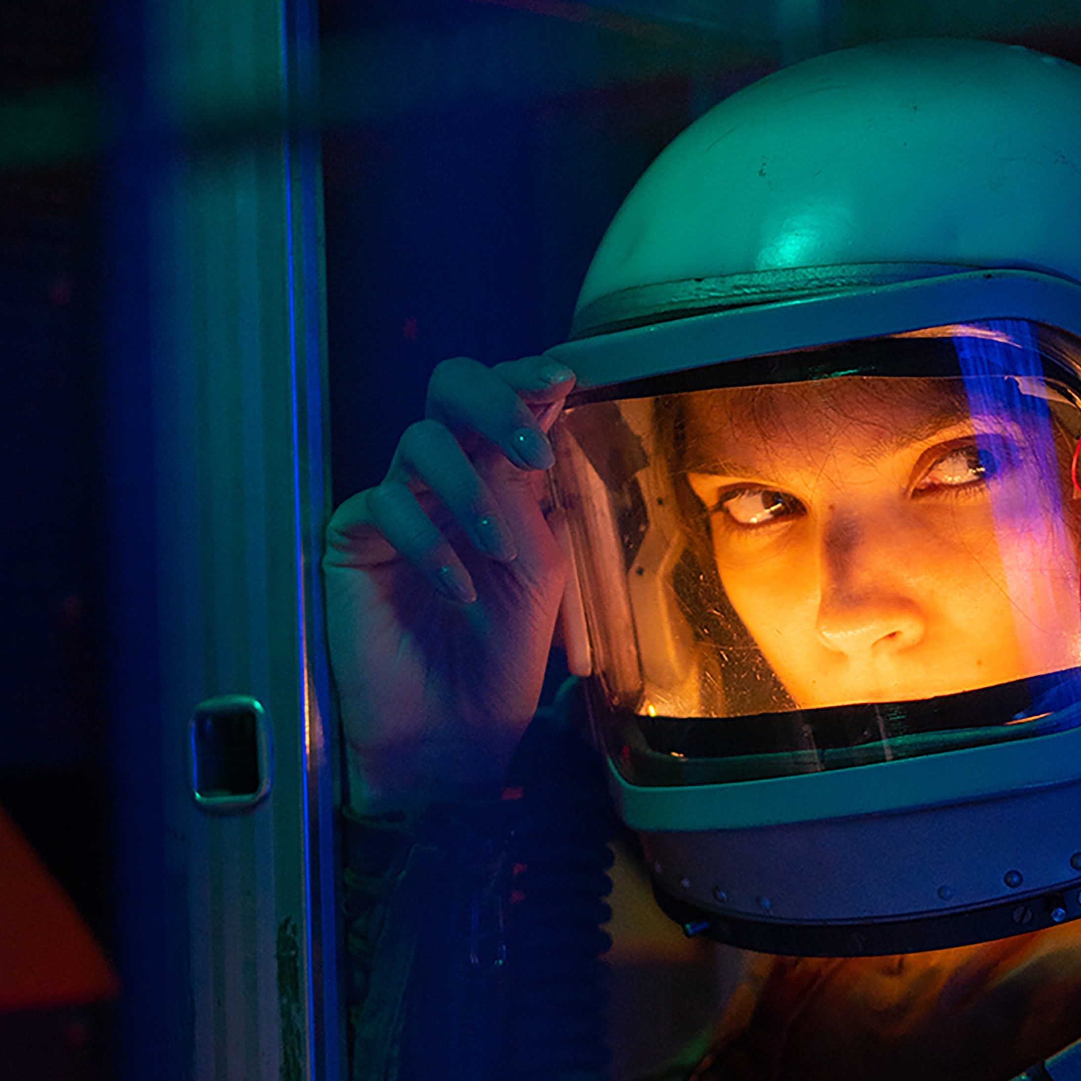 A female astronaut wearing a space helmet, which is lit up from the inside.